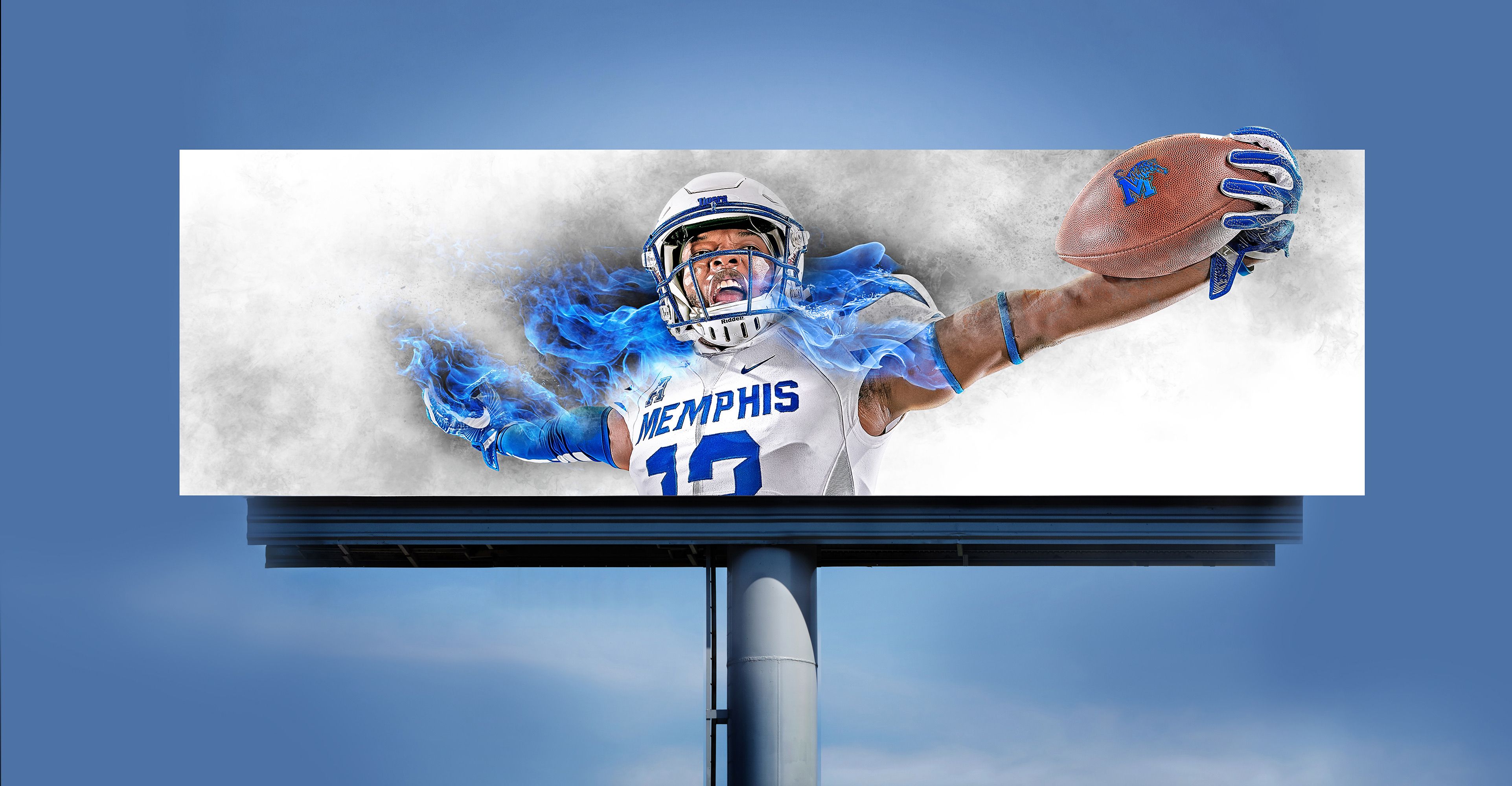 Outdoor billboard showing Memphis Tigers wide receiver #12 stretching one-handed to catch a football, blue fire trailing his arm, set against a blue sky.