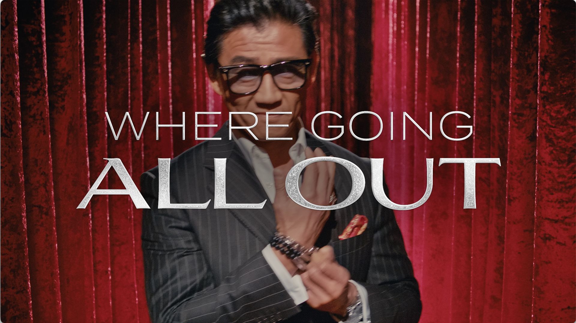 Man in a pinstripe suit adjusting his cuff, with the text 'WHERE GOING ALL OUT' superimposed over red velvet curtains.